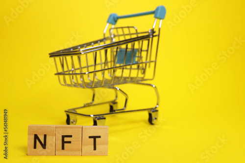 word NFT from wooden blocks on the background of a supermarket trolley. The concept of investment, NFT purchases