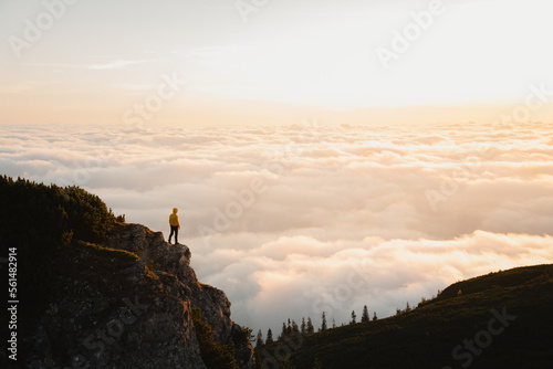 One person hiker standing above mountain cliff looking at view above the clouds at sunrise or sunset at Ceahlau Masiff. Travel, hiking and succes concept