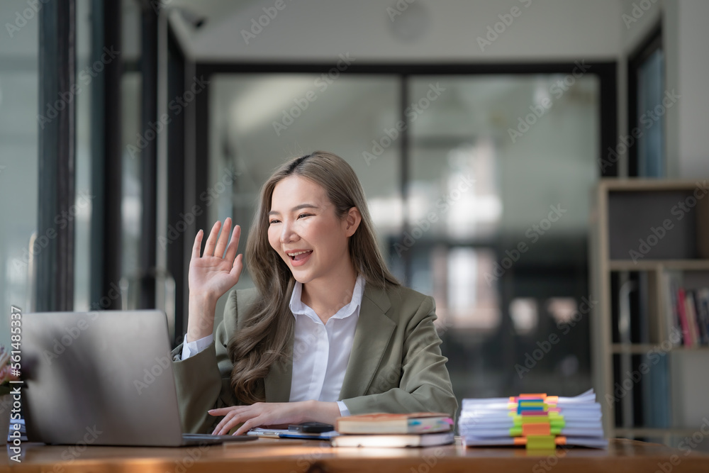 Smiling professional Asian businesswoman talking in front of the camera while having a video conference with her business partners on a laptop in a contemporary office space. Smiling professional Asian businesswoman talking in front of the camera while having a video conference with her business partners on a laptop in a contemporary office space.