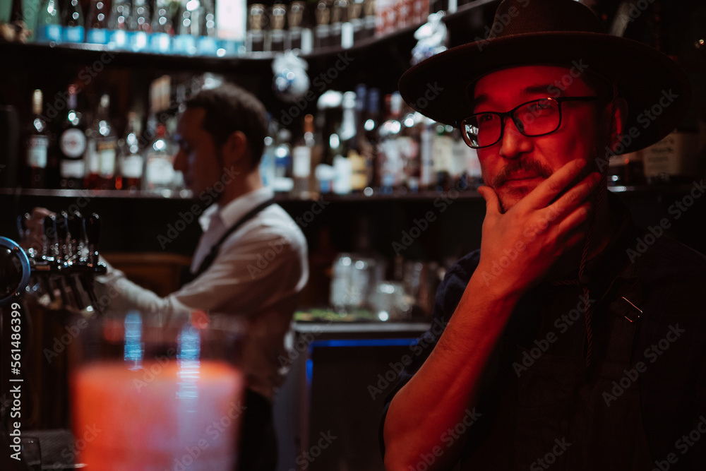 portrait of a bearded bartender in a hat in bar against the background of bottles of alcohol portrait of a bearded bartender in a hat in bar against the background of bottles of alcohol