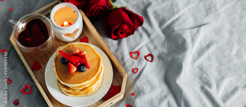Pancakes in the shape of a heart with berries, roses flowers, cup of tea and candle in candlestick. Valentine's day breakfast concept. Top view with copy space. Banner for design, web site