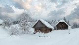 Two wooden sheds in snowdrifts on the slopes in winter Ukrainian Carpathian Mountains in cloudy weather.