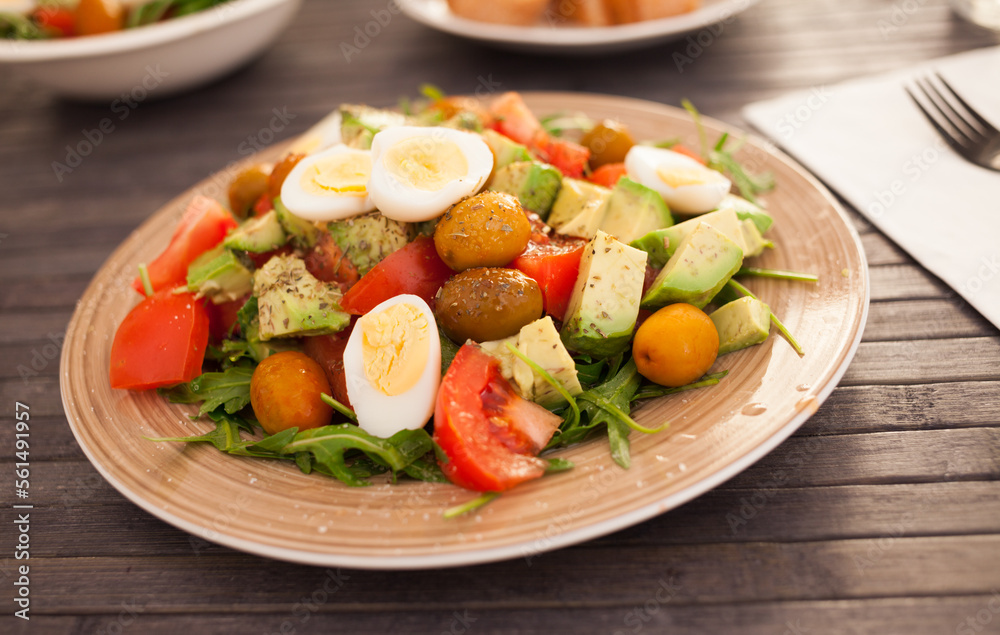 fresh salad of arugula, avocado, cherry tomatoes with olives and quail eggs on brown plate fresh salad of arugula, avocado, cherry tomatoes with olives and quail eggs on brown plate