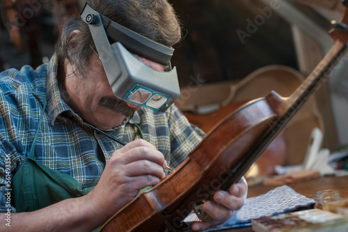 Violin maker painting violin using magnification