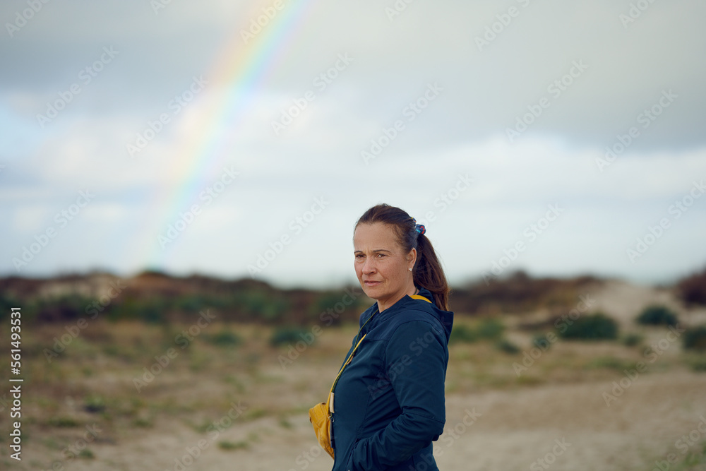 Middle-aged woman looking thoughtful at the camera with a rainbow in the background, concept for future outlook Middle-aged woman looking thoughtful at the camera with a rainbow in the background, concept for future outlook