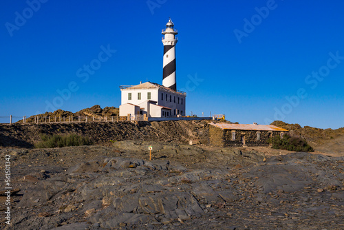 The lighthouse at Cape Favaritx amid dark slate rock, Menorca, Spain photo