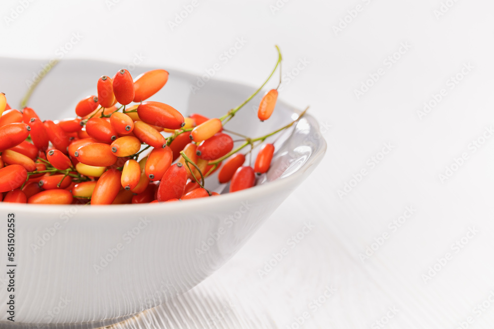 Red barberry berries in ceramic plate on wooden table, selective focus, white background, copy space. Ripe fresh sour-tasting berries, healthy and seasoning for food. Natural Barberry twigs Red barberry berries in ceramic plate on wooden table, selective focus, white background, copy space. Ripe fresh sour-tasting berries, healthy and seasoning for food. Natural Barberry twigs