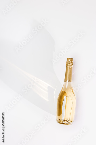 Top view white sparkling wine bottle with sunlight shadow and glare on light white gray background. Vertical flat lay, one champagne bottle, non-alcoholic drinks, minimal style still life.