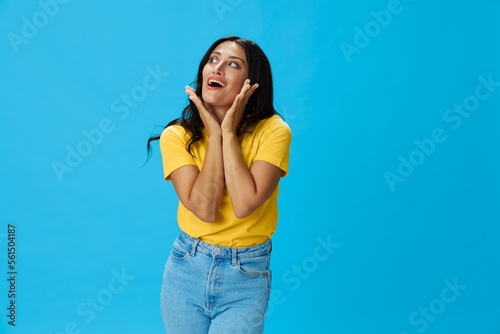 Woman in yellow t-shirt on blue background posing gestures emotions and signals with smile, hands up happiness copy space