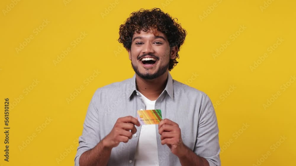 Young Indian man 20s wear casual grey shirt hold in hand pointing index finger on mockup plastic credit bank card showing thumb up isolated on plain yellow background studio. People lifestyle concept Young Indian man 20s wear casual grey shirt hold in hand pointing index finger on mockup plastic credit bank card showing thumb up isolated on plain yellow background studio. People lifestyle concept