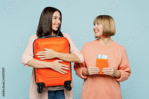 Elder parent mom young adult daughter two women in casual clothes hold passport ticket valise isolated on plain blue background Tourist travel abroad in free time rest getaway Air flight trip concept photo