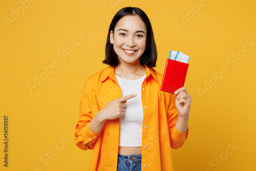 Young woman wear summer casual clothes hold point finger on passport ticked isolated on plain yellow background. Tourist travel abroad in free spare time rest getaway. Air flight trip journey concept. #561511387