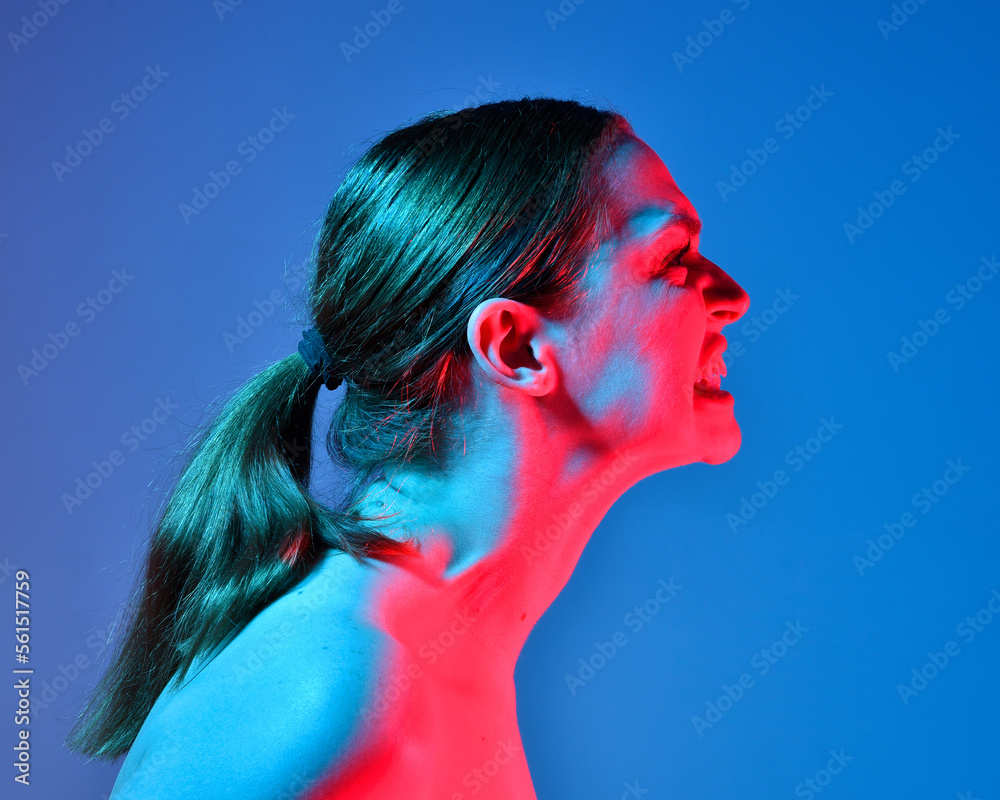 Naklejka premium Head and shoulders close up portrait of pretty girl with expressive facial expressions, with colourful neon gel lighting, isolated on studio background.