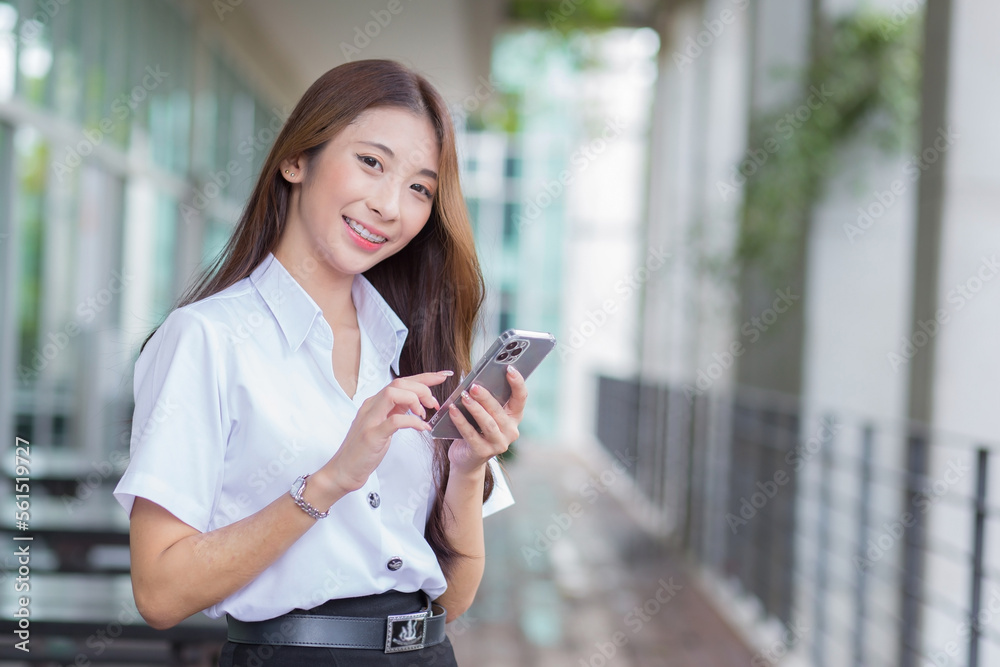 Portrait of cute Asian Thai girl student in uniform is standing work smiling happily and confidently while using smartphone in the building at university with background. Portrait of cute Asian Thai girl student in uniform is standing work smiling happily and confidently while using smartphone in the building at university with background.