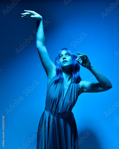 close up portrait of pretty girl with blue hair wig and elegant gown, with expressive facial expressions and gestural arm poseswith colourful neon gel lighting, isolated on studio background.