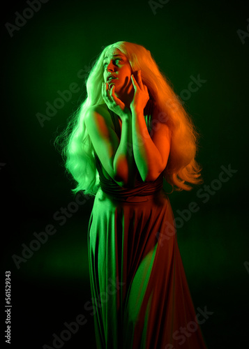 portrait of pretty girl with blonde hair & elegant gown with expressive facial expressions & gestural arm poses. colourful neon gel lighting, isolated on black studio background.