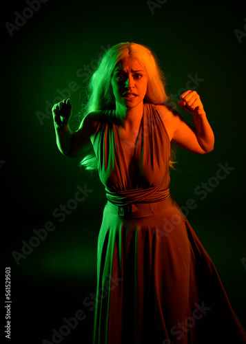 portrait of pretty girl with blonde hair & elegant gown with expressive facial expressions & gestural arm poses. colourful neon gel lighting, isolated on black studio background.