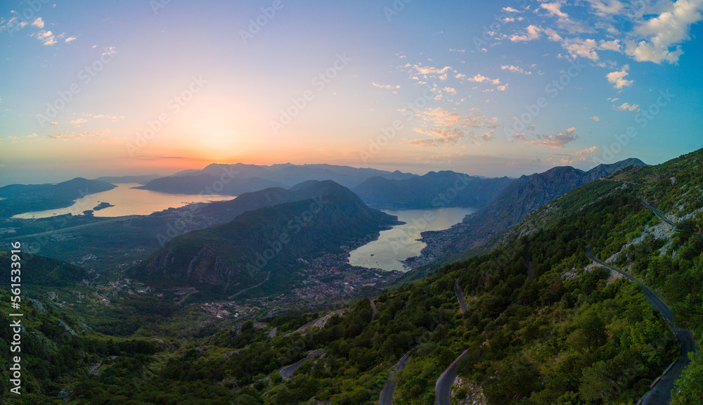 Panorama of dazzling sun in the evening sky illuminates all the peaks of the Balkan Montenegrin mountains and the coast of Kotor Bay