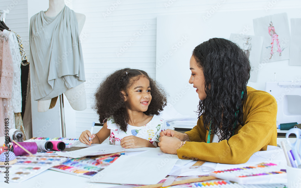 Beautiful adult mother teaching, bonding her mixed race African little cute daughter girl using sewing machine for making dress, clothes at home or tailor shop, smiling with happiness together.