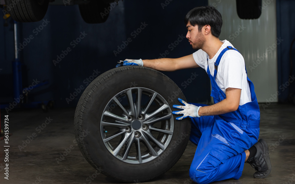 Asian male mechanic wearing uniform, changing rubber tyre or tire wheel, working in garage at car or automobile maintenance service center or shop. Industry Concept. Asian male mechanic wearing uniform, changing rubber tyre or tire wheel, working in garage at car or automobile maintenance service center or shop. Industry Concept.