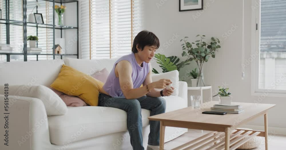 Young adult real gay LGBT man pouring bottle take pill drink water glass sit at home sofa couch. Gen Z asia people LGBTQ male or non binary gender happy smile eat beauty skin health care medical drug. Young adult real gay LGBT man pouring bottle take pill drink water glass sit at home sofa couch. Gen Z asia people LGBTQ male or non binary gender happy smile eat beauty skin health care medical drug.