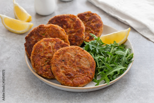Tuna Patties or small fish cakes made with canned tuna, white beans, herbs and potato served on a plate with arugula salad and lemon wedges. Selective focus, gray concrete background. Horizontal. photo