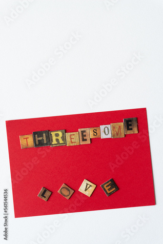 the words "threesome love" composed of chipboard tiles with vintage style letters on a red card (and isolated on blank paper)