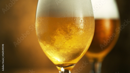 Glass of light beer on dark golden background.
