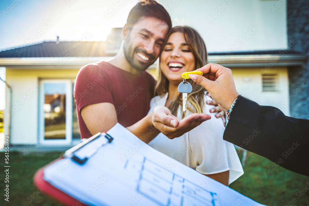 Happy millennial couple receiving keys from realtor, purchasing real estate - Family meeting with real estate agent - New house and real estate concept - obrazy, fototapety, plakaty 