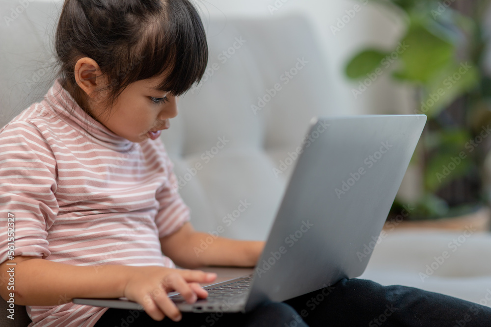 Asian Little school kid girl use laptop computer sitting on sofa alone at home. Child learning reading online social media content, play education lessons game chatting with friends. Asian Little school kid girl use laptop computer sitting on sofa alone at home. Child learning reading online social media content, play education lessons game chatting with friends.