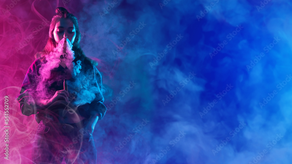 Obraz premium Woman vaper. Girl with electronic cigarette in smoke. Female student smokes vape. Lady with vaping device. Hipster model blows smoke from nose. Vape device in female hand. Woman vaper in neon light