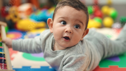 Adorable hispanic baby lying on floor with relaxed expression at kindergarten