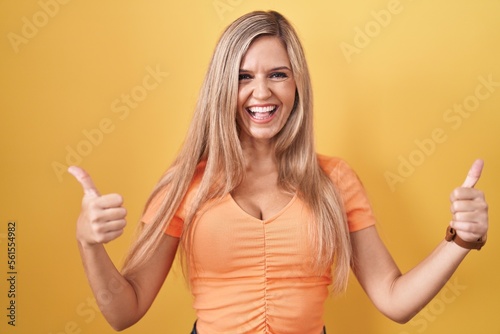 Young woman standing over yellow background success sign doing positive gesture with hand, thumbs up smiling and happy. cheerful expression and winner gesture.