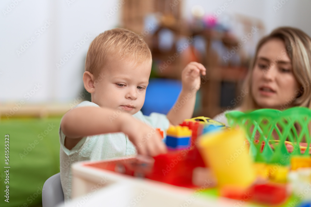 Teacher and toddler playing with construction blocks sitting on table at kindergarten Teacher and toddler playing with construction blocks sitting on table at kindergarten
