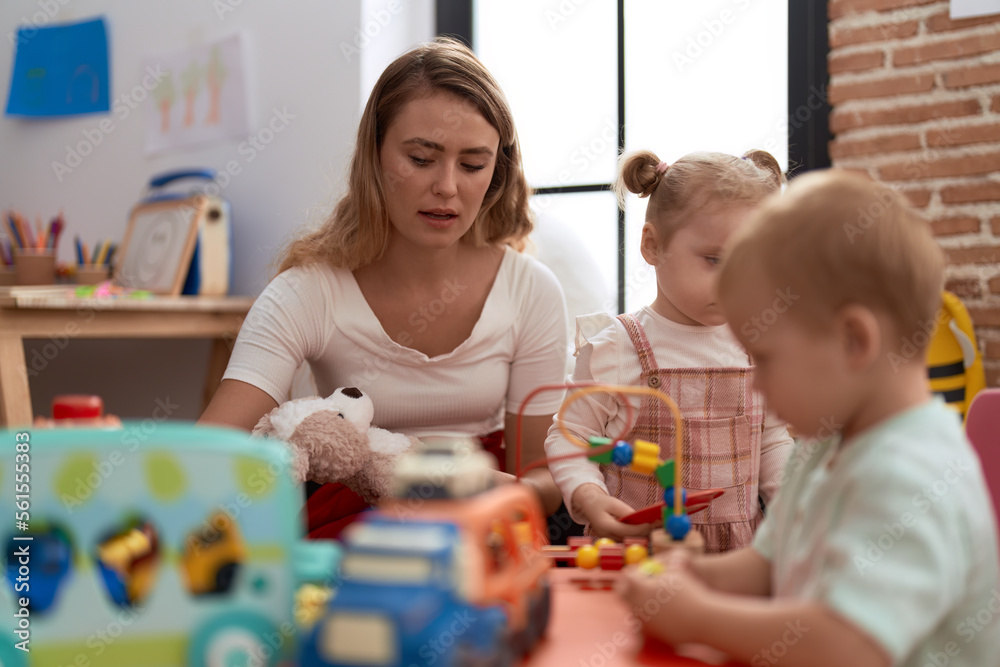 Teacher with boy and girl playing with toys sitting on table at kindergarten Teacher with boy and girl playing with toys sitting on table at kindergarten