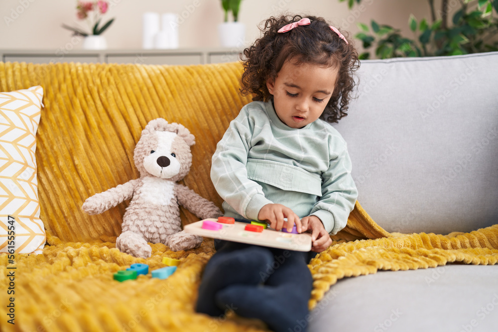 Adorable hispanic girl playing maths game sitting on sofa at home Adorable hispanic girl playing maths game sitting on sofa at home