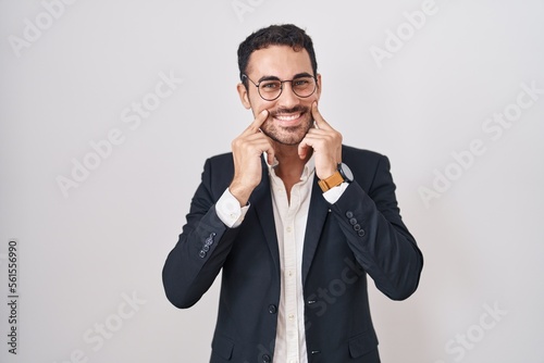 Handsome business hispanic man standing over white background smiling with open mouth, fingers pointing and forcing cheerful smile