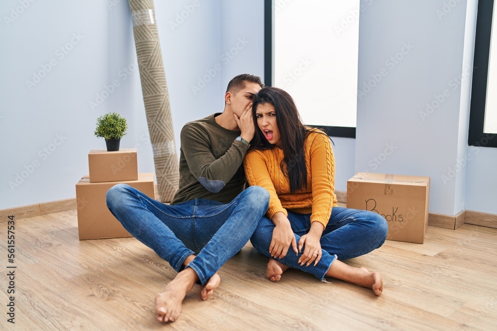 Young couple sitting on the floor at new home hand on mouth telling secret rumor, whispering malicious talk conversation Young couple sitting on the floor at new home hand on mouth telling secret rumor, whispering malicious talk conversation