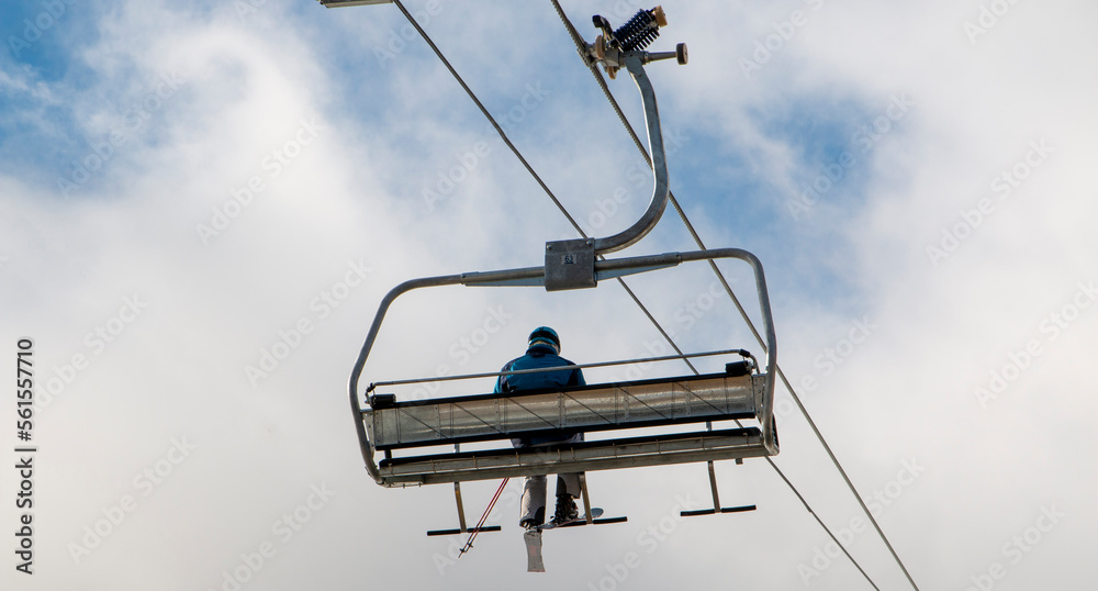 One skier riding on a skilift with clouds and a little blue sky One skier riding on a skilift with clouds and a little blue sky