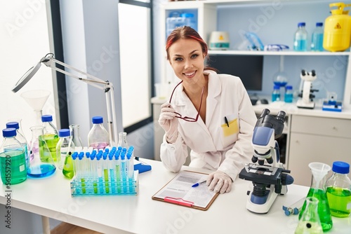 Young caucasian woman scientist smiling confident holding glasses at laboratory