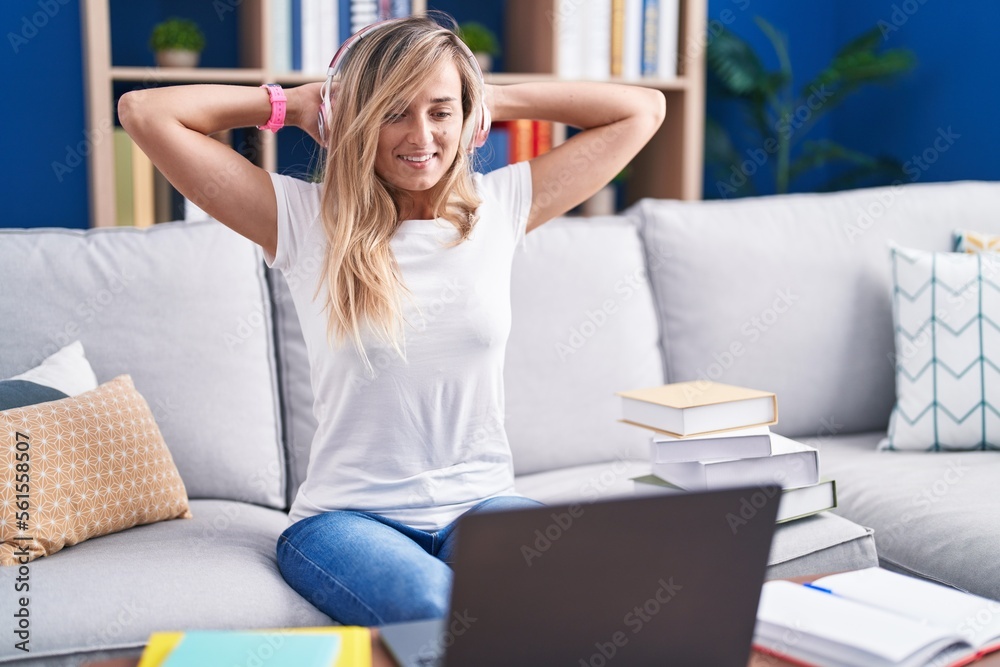 Young blonde woman studying using computer laptop at home relaxing and stretching, arms and hands behind head and neck smiling happy Young blonde woman studying using computer laptop at home relaxing and stretching, arms and hands behind head and neck smiling happy
