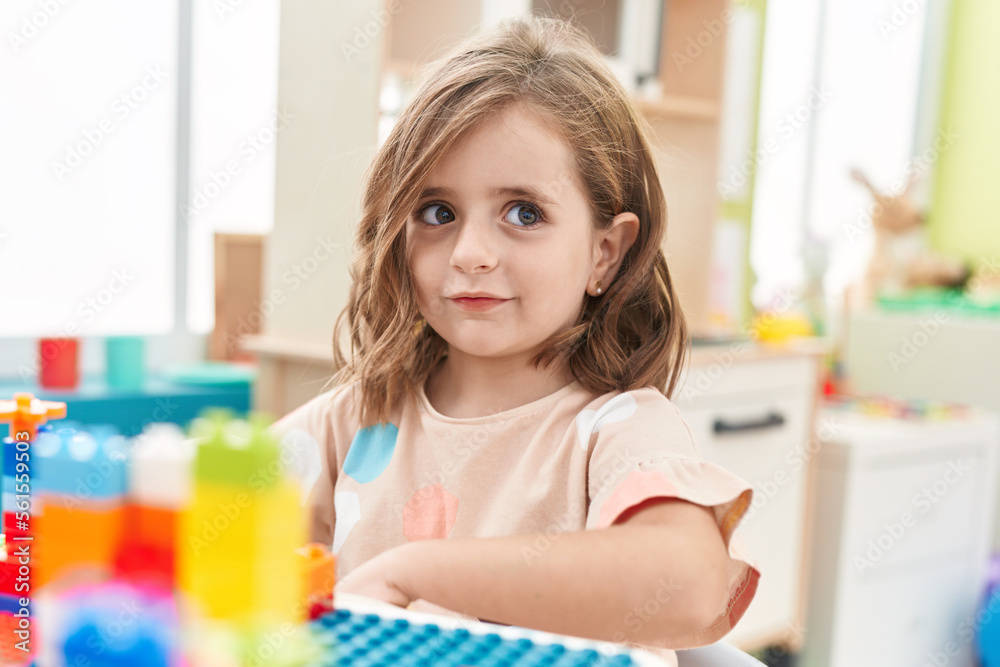 Adorable hispanic girl playing with construction blocks sitting on table at kindergarten Adorable hispanic girl playing with construction blocks sitting on table at kindergarten
