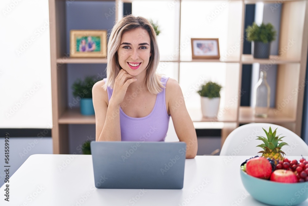 Young woman using laptop sitting on table at home Young woman using laptop sitting on table at home