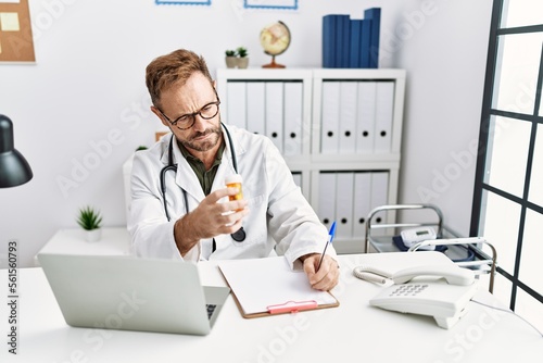 Middle age hispanic man wearing doctor uniform holding pills at clinic