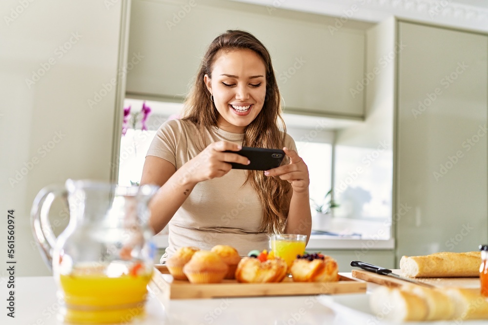 Young beautiful hispanic woman make photo by smartphone to breakfast at the kitchen