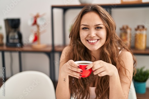 Young beautiful hispanic woman drinking coffee sitting on table at home
