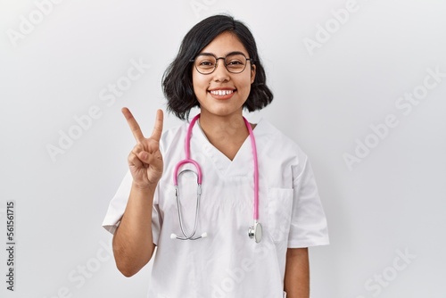 Young hispanic doctor woman wearing stethoscope over isolated background showing and pointing up with fingers number two while smiling confident and happy.