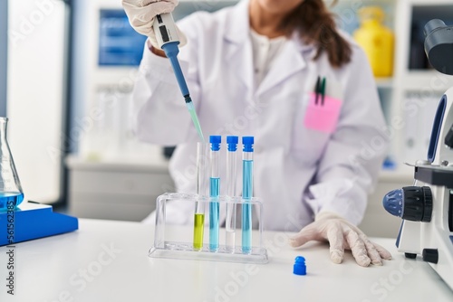 Young latin woman wearing scientist uniform using pipette working at laboratory