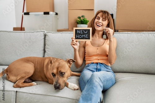 Young caucasian woman holding key and new home blackboard sitting on sofa with dog at home