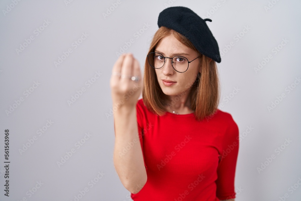 Young redhead woman standing wearing glasses and beret doing italian gesture with hand and fingers confident expression Young redhead woman standing wearing glasses and beret doing italian gesture with hand and fingers confident expression